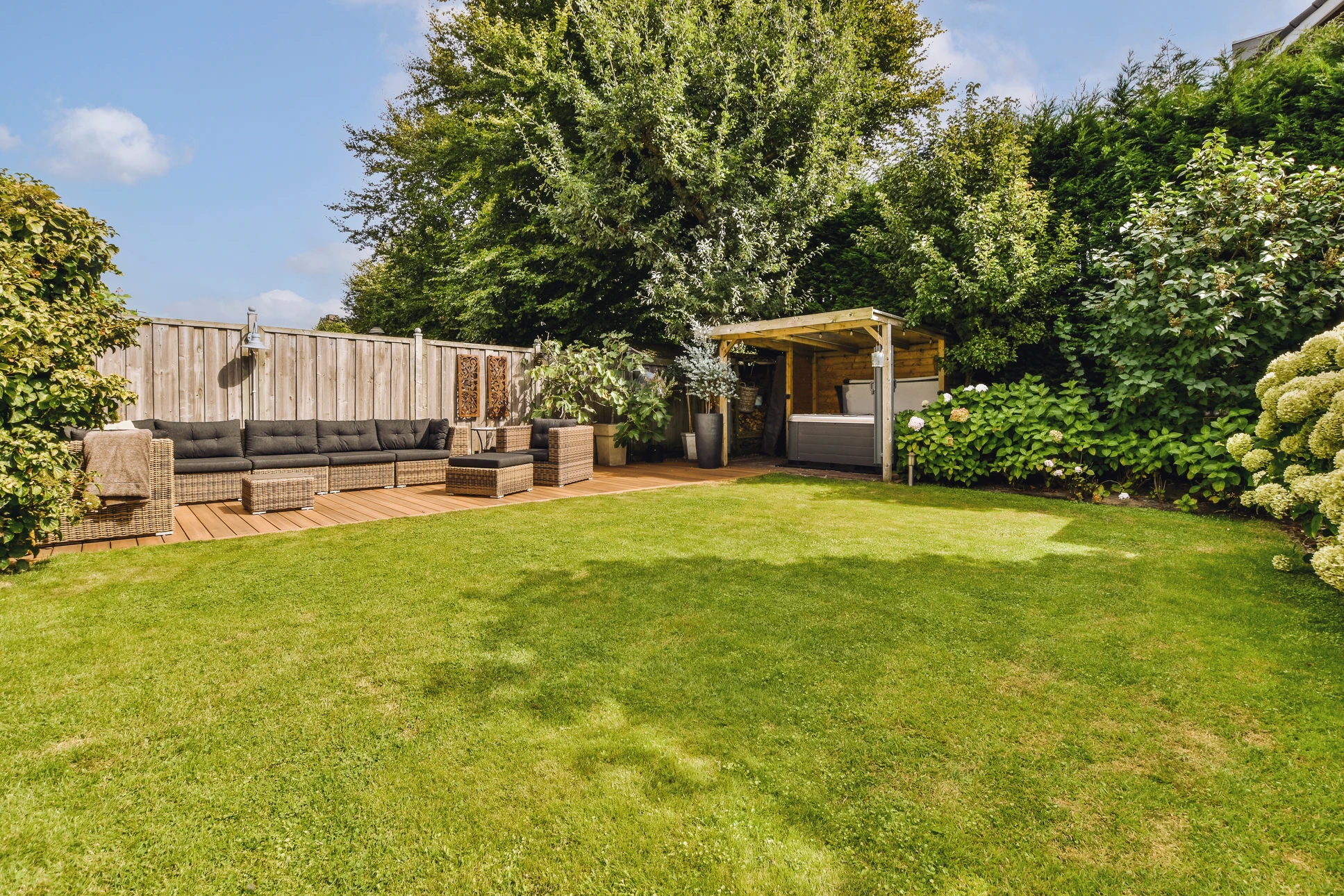 Jardin privé avec salon de jardin en bois naturel disposé sous un grand arbre feuillu